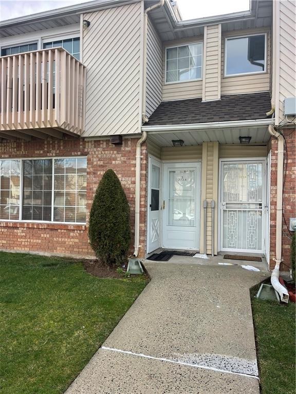 entrance to property with brick siding, a yard, a balcony, and roof with shingles