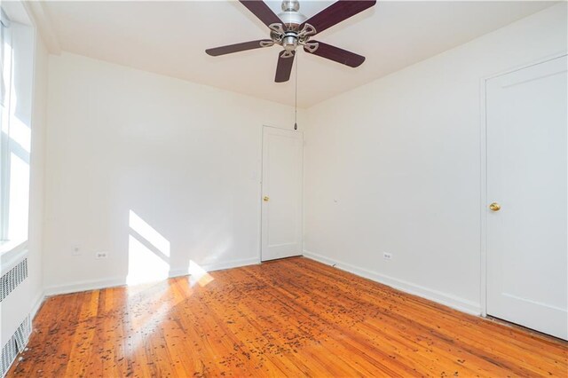 spare room featuring radiator, ceiling fan, a healthy amount of sunlight, and wood-type flooring