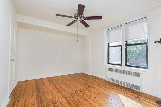 empty room with ceiling fan, radiator heating unit, and hardwood / wood-style flooring