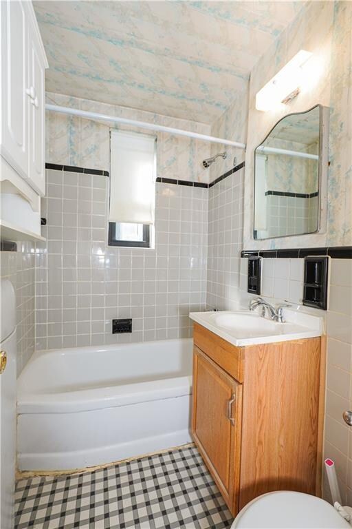 full bathroom with toilet, vanity, tile patterned flooring, tile walls, and tiled shower / bath combo