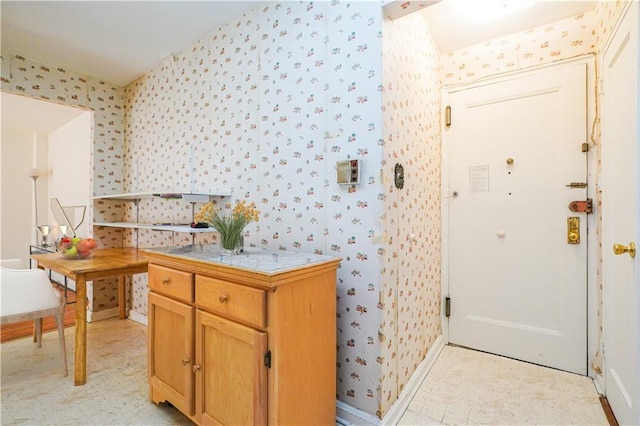 kitchen featuring tile counters, baseboards, light floors, and wallpapered walls