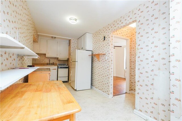 kitchen with wood counters, white cabinetry, white fridge, sink, and stove