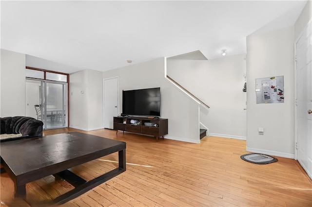 living area with light wood-type flooring, baseboards, and stairs