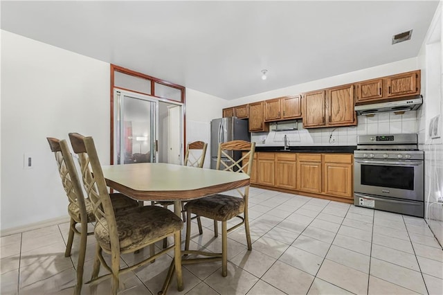 547 Sheffield Ave, Brooklyn, NY 11207 - kitchen featuring appliances with stainless steel finishes, under cabinet range hood, dark countertops, tasteful backsplash, and brown cabinetry
