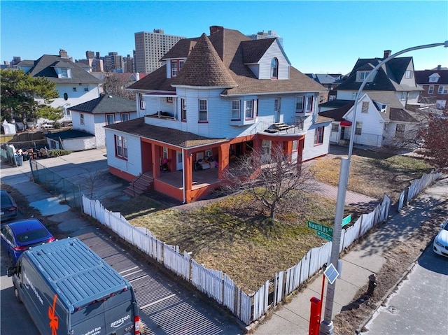 view of front of property featuring a fenced front yard, a residential view, concrete driveway, and a shingled roof