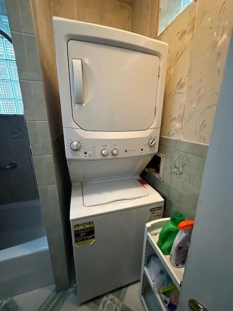 washroom featuring stacked washing maching and dryer and tile walls