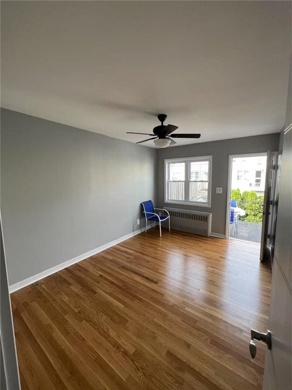 unfurnished room featuring ceiling fan, baseboards, radiator, and wood finished floors