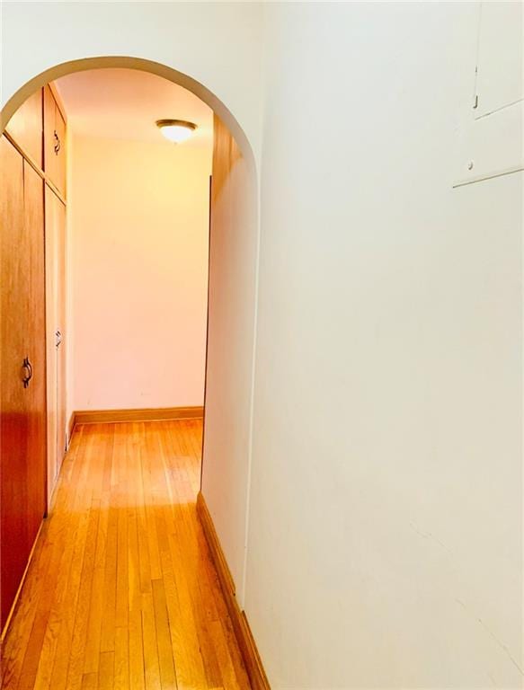 hall featuring light wood-style floors, baseboards, and arched walkways