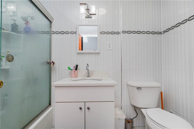 full bathroom with enclosed tub / shower combo, vanity, tile walls, and toilet