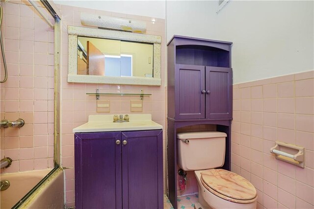 full bathroom featuring vanity, combined bath / shower with glass door, tile walls, and toilet