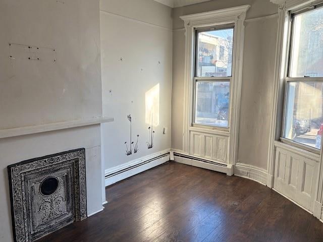 unfurnished living room with a baseboard heating unit, dark hardwood / wood-style flooring, and a healthy amount of sunlight