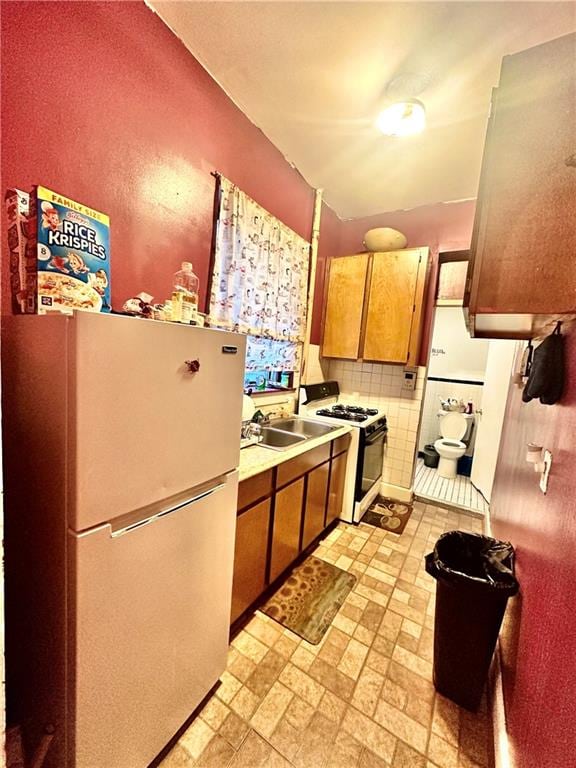 kitchen featuring white refrigerator, sink, range with gas stovetop, and decorative backsplash