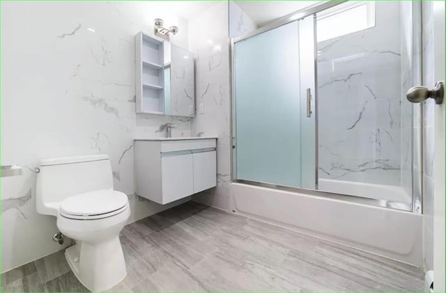 full bathroom featuring toilet, combined bath / shower with glass door, tile walls, and vanity