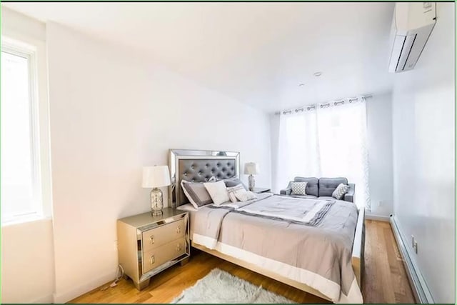 bedroom with light wood-type flooring, a wall mounted air conditioner, and a baseboard radiator