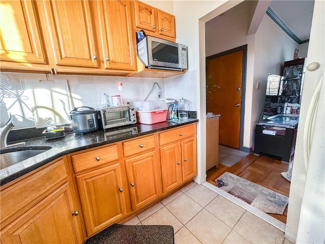 kitchen featuring sink, crown molding, light tile patterned floors, dark stone countertops, and decorative backsplash