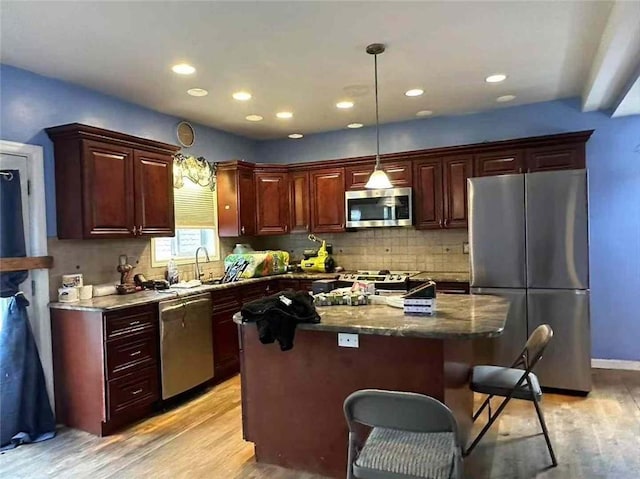 kitchen featuring hanging light fixtures, dark stone counters, light wood-type flooring, a kitchen island, and stainless steel appliances