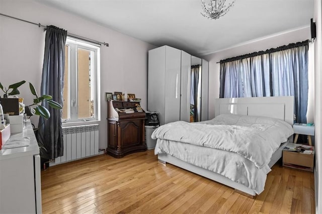 bedroom with radiator, multiple windows, and light wood finished floors