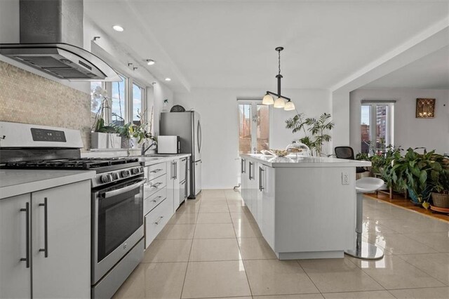 kitchen with island range hood, a center island with sink, appliances with stainless steel finishes, pendant lighting, and white cabinets