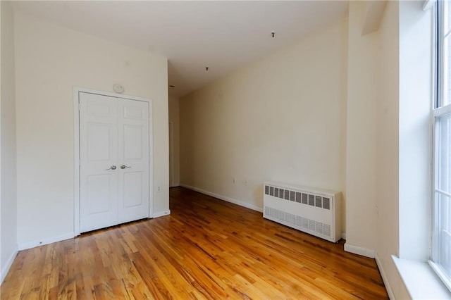 unfurnished bedroom featuring light hardwood / wood-style floors, multiple windows, radiator, and a closet