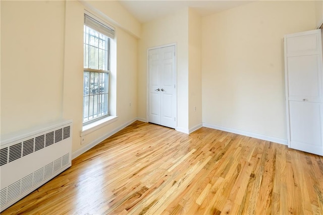 unfurnished bedroom with light hardwood / wood-style floors and radiator heating unit