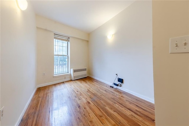 empty room featuring lofted ceiling, light hardwood / wood-style flooring, and radiator heating unit