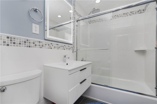 bathroom featuring vanity, toilet, tile walls, recessed lighting, and bath / shower combo with glass door