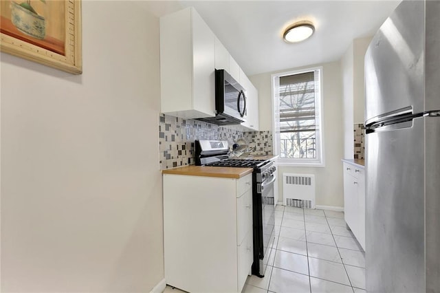 kitchen with radiator, light tile patterned floors, backsplash, stainless steel appliances, and white cabinets