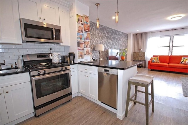 1000 Clove Rd Unit 7G, Staten Island, NY 10301 - kitchen featuring appliances with stainless steel finishes, a peninsula, dark countertops, light wood-style flooring, and wallpapered walls