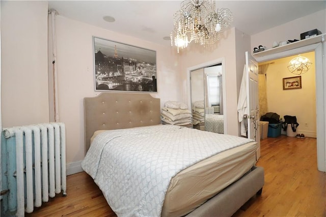 bedroom with wood-type flooring, radiator heating unit, an inviting chandelier, and a closet