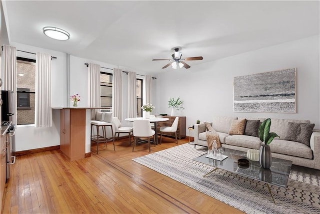 living room featuring baseboards, ceiling fan, and light wood finished floors