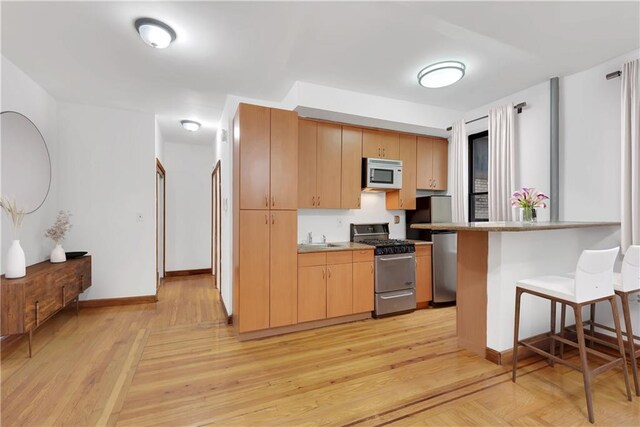 kitchen with stainless steel range with gas cooktop, sink, a kitchen breakfast bar, light hardwood / wood-style floors, and kitchen peninsula