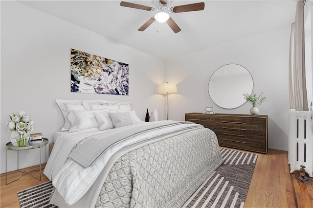 bedroom with ceiling fan, radiator heating unit, and wood-type flooring