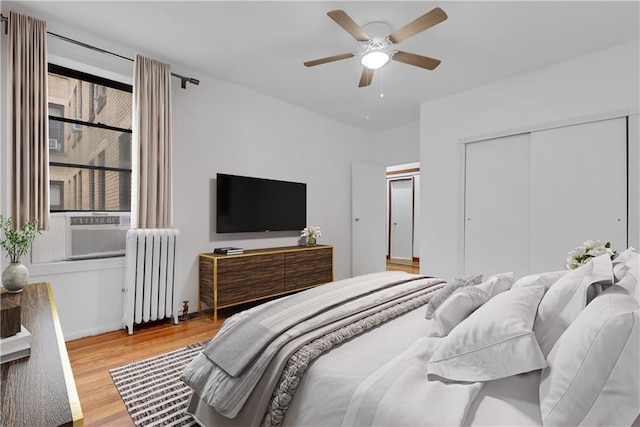 bedroom featuring a closet, radiator, ceiling fan, wood finished floors, and cooling unit