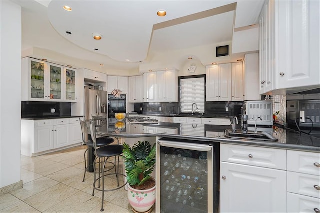 kitchen with beverage cooler, white cabinetry, black oven, and dark countertops