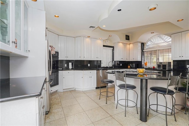 kitchen featuring a breakfast bar, white cabinets, dishwasher, and backsplash