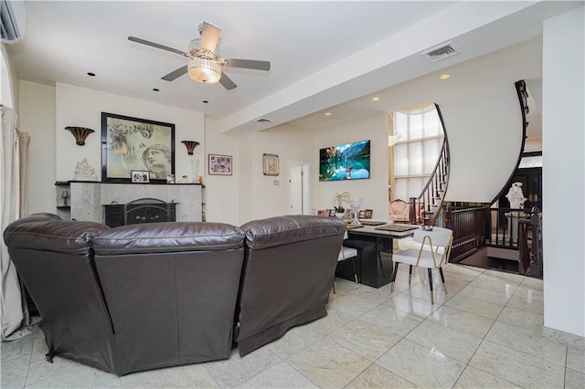 living room with a fireplace, an AC wall unit, a ceiling fan, visible vents, and stairway