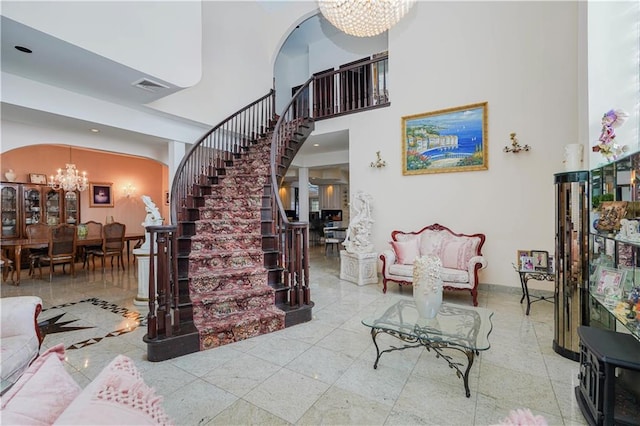 living room with an inviting chandelier, visible vents, a towering ceiling, baseboards, and stairway