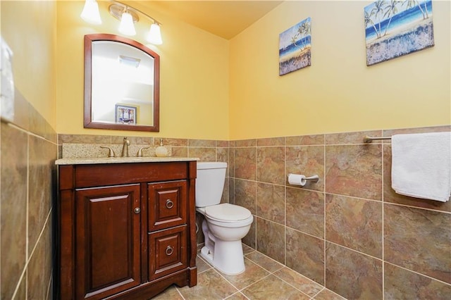 half bath with vanity, toilet, tile walls, tile patterned floors, and a wainscoted wall