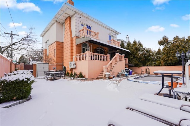 snow covered back of property featuring stairway, fence, a chimney, and outdoor dining area