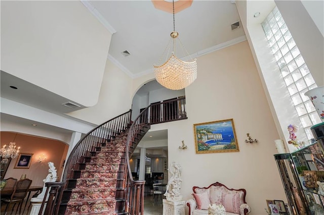 stairs with ornamental molding, visible vents, and an inviting chandelier