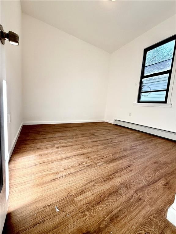 empty room featuring hardwood / wood-style flooring and a baseboard heating unit