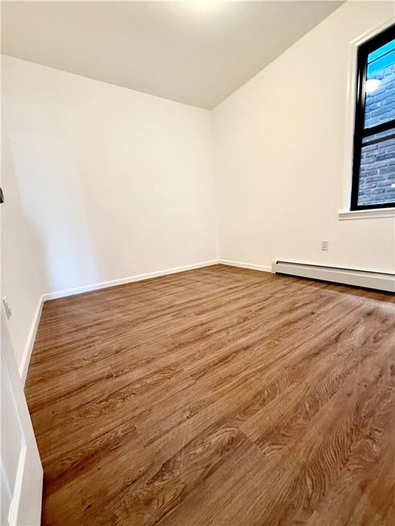 empty room with wood-type flooring and a baseboard radiator