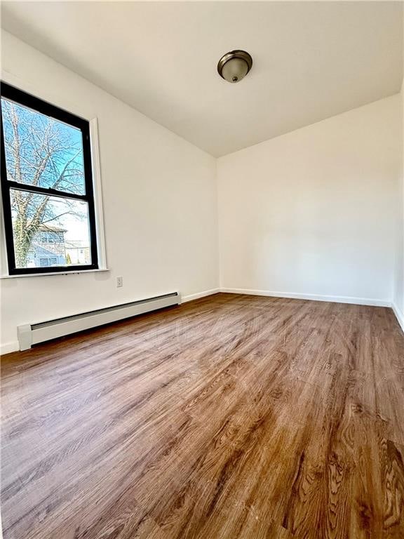 unfurnished room with a baseboard heating unit and wood-type flooring