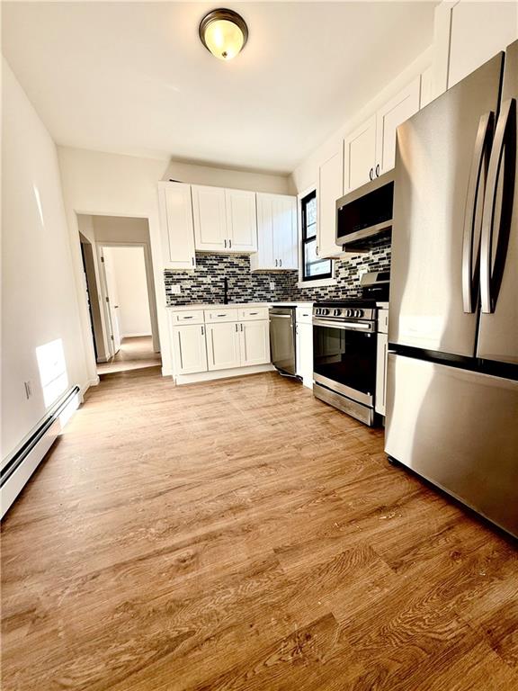 kitchen featuring white cabinetry, light wood-type flooring, tasteful backsplash, and appliances with stainless steel finishes