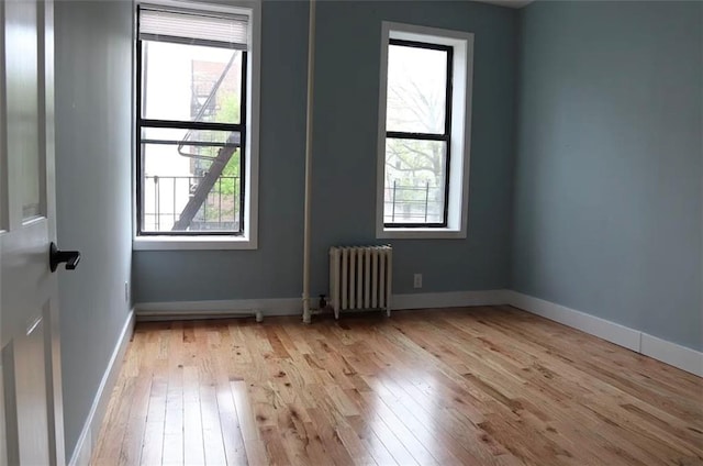 unfurnished room with a healthy amount of sunlight, radiator, and light wood-type flooring