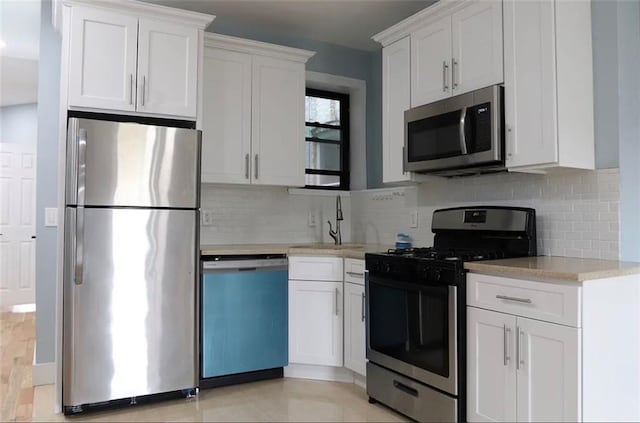 kitchen with stainless steel appliances, white cabinetry, sink, and backsplash