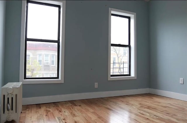 unfurnished room with baseboards, light wood-style floors, and radiator heating unit