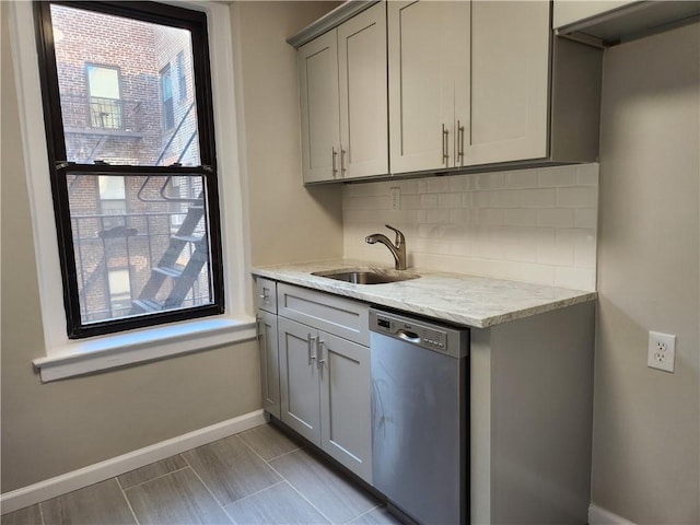 kitchen featuring stainless steel dishwasher, a sink, baseboards, decorative backsplash, and gray cabinetry