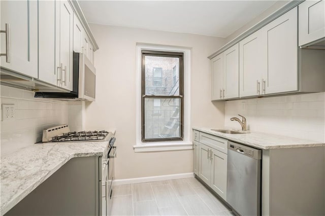 kitchen featuring a sink, decorative backsplash, stainless steel appliances, baseboards, and light stone countertops