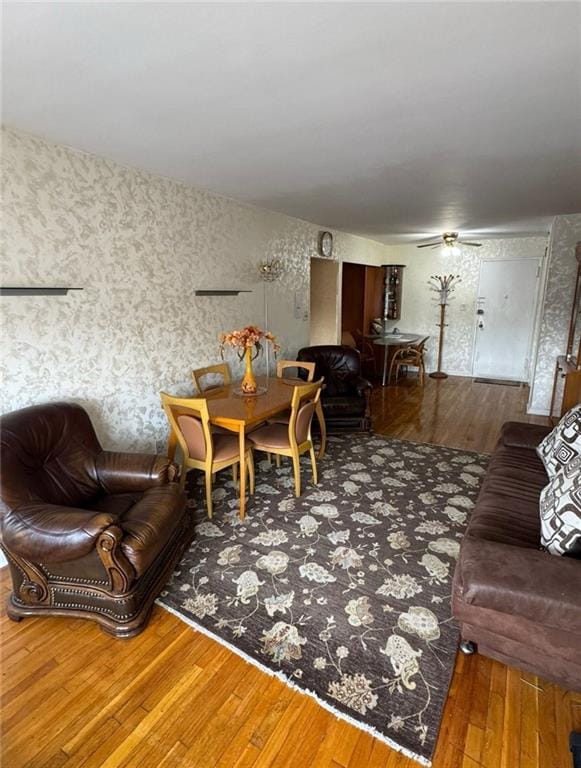 living room with wallpapered walls, a ceiling fan, and wood finished floors